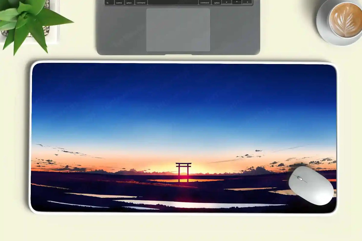 Custom desk mat with sunset and torii gate design, placed under laptop with white mouse and coffee cup